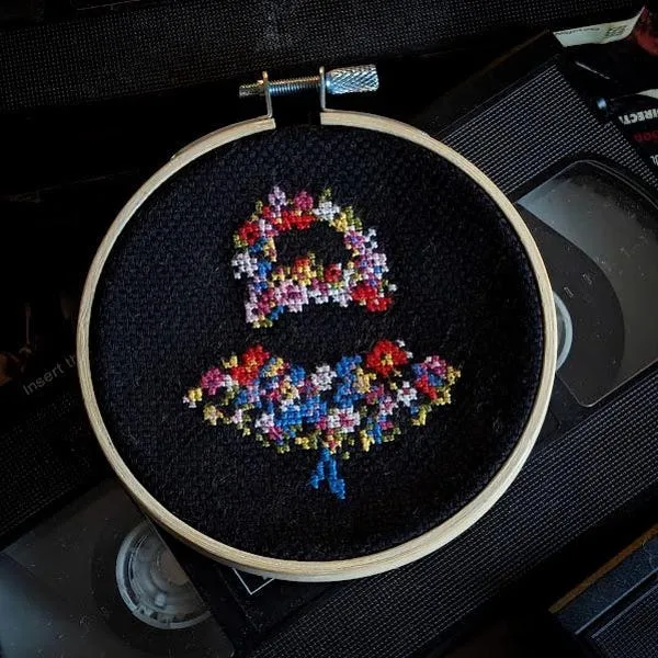 A finished floral skull cross stitch on black fabric surrounded by vintage media