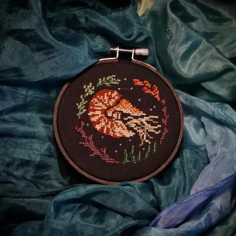 Nautilus cross stitch with orange and cream threads on black fabric